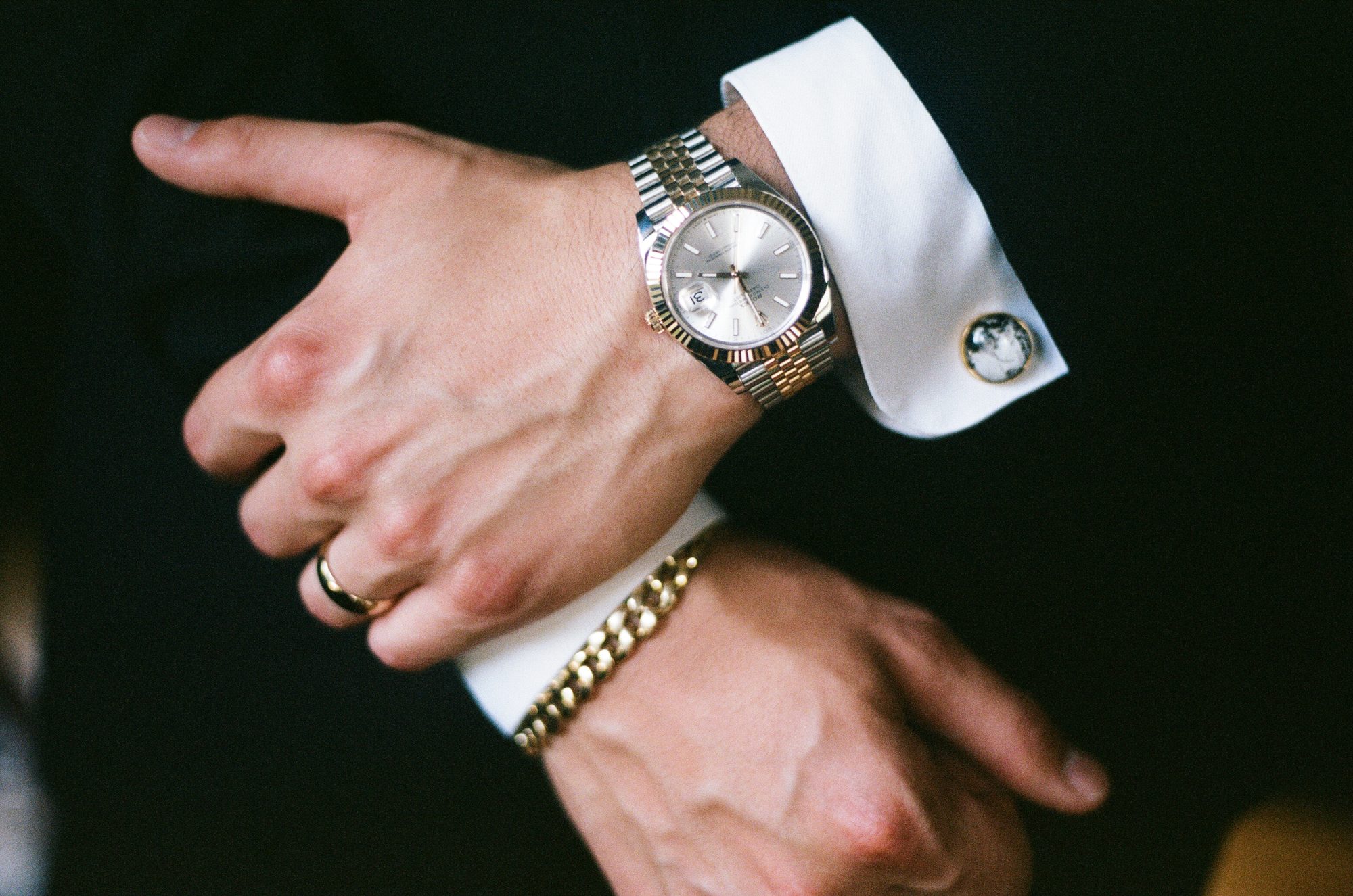 Close detail of a groom's hands showing a gold watch, cufflink, ring, and bracelet.