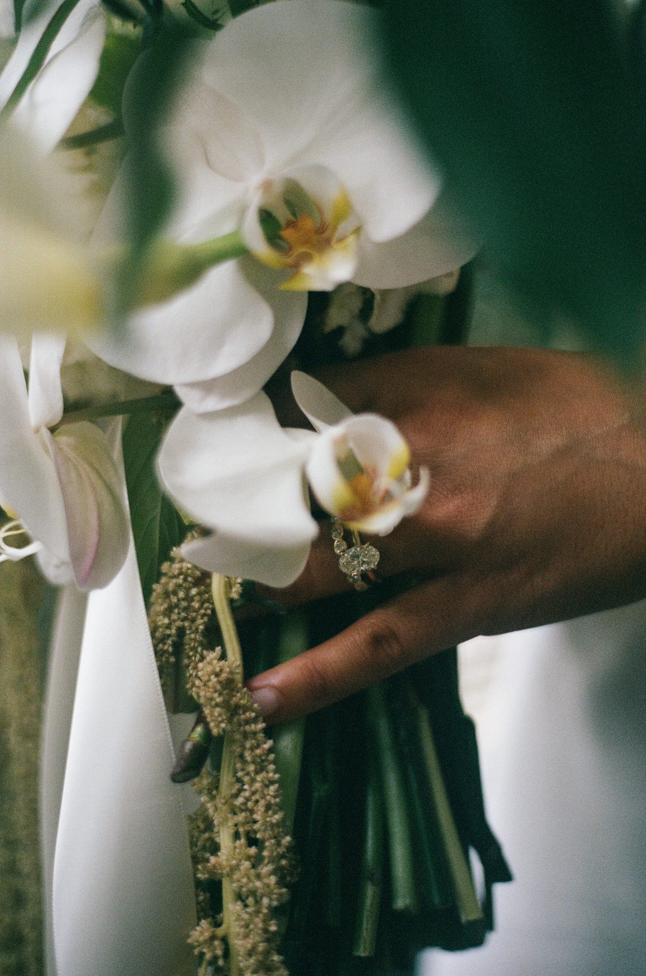 Close detail of white orchids in a bouquet with an engagement ring visible on a hand tucked among the flowers.
