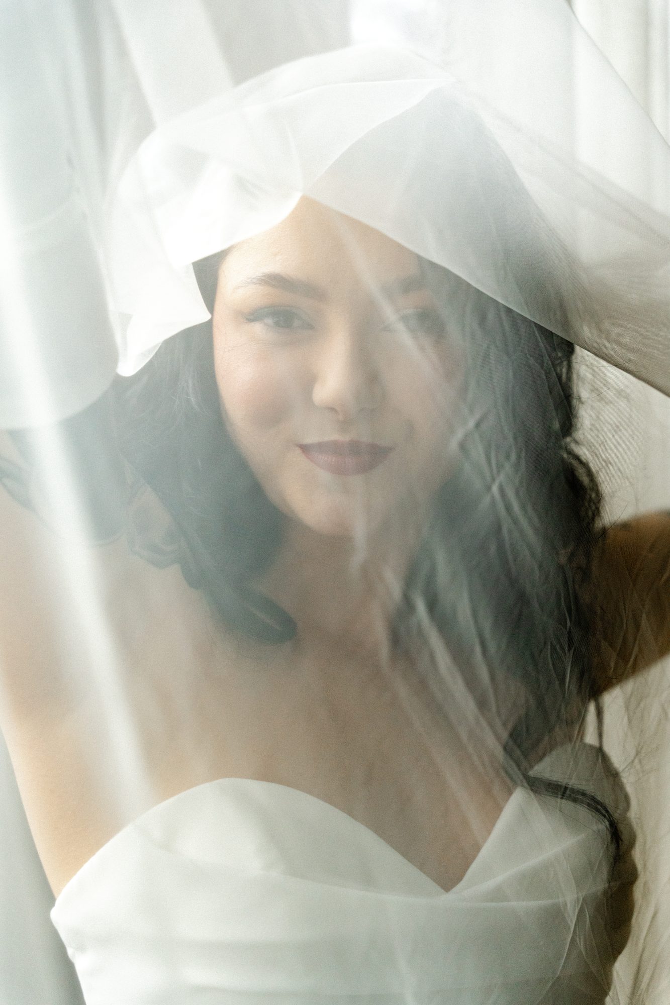 A soft-focus portrait of a bride smiling through a sheer veil.