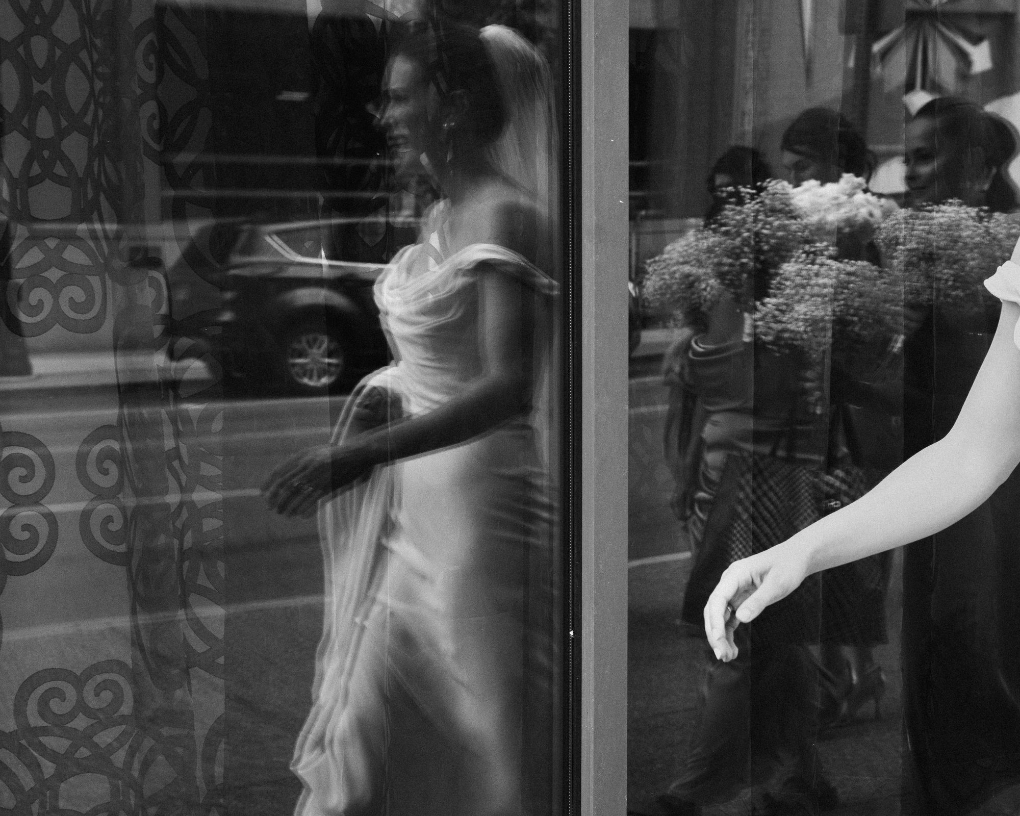 A bride reflected in a storefront window on a city street, double-exposure effect.