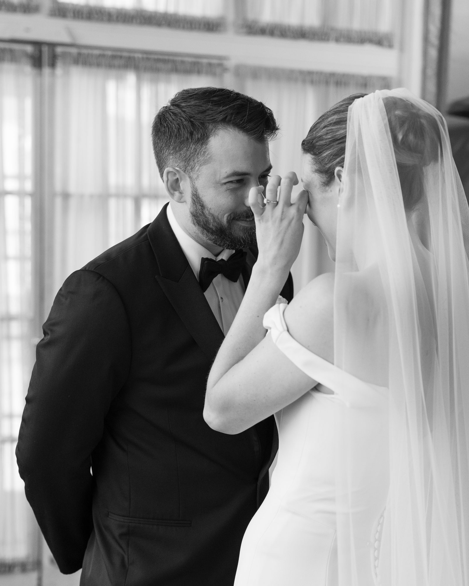 A groom wiping a tear from his bride's cheek during their first look, black and white.