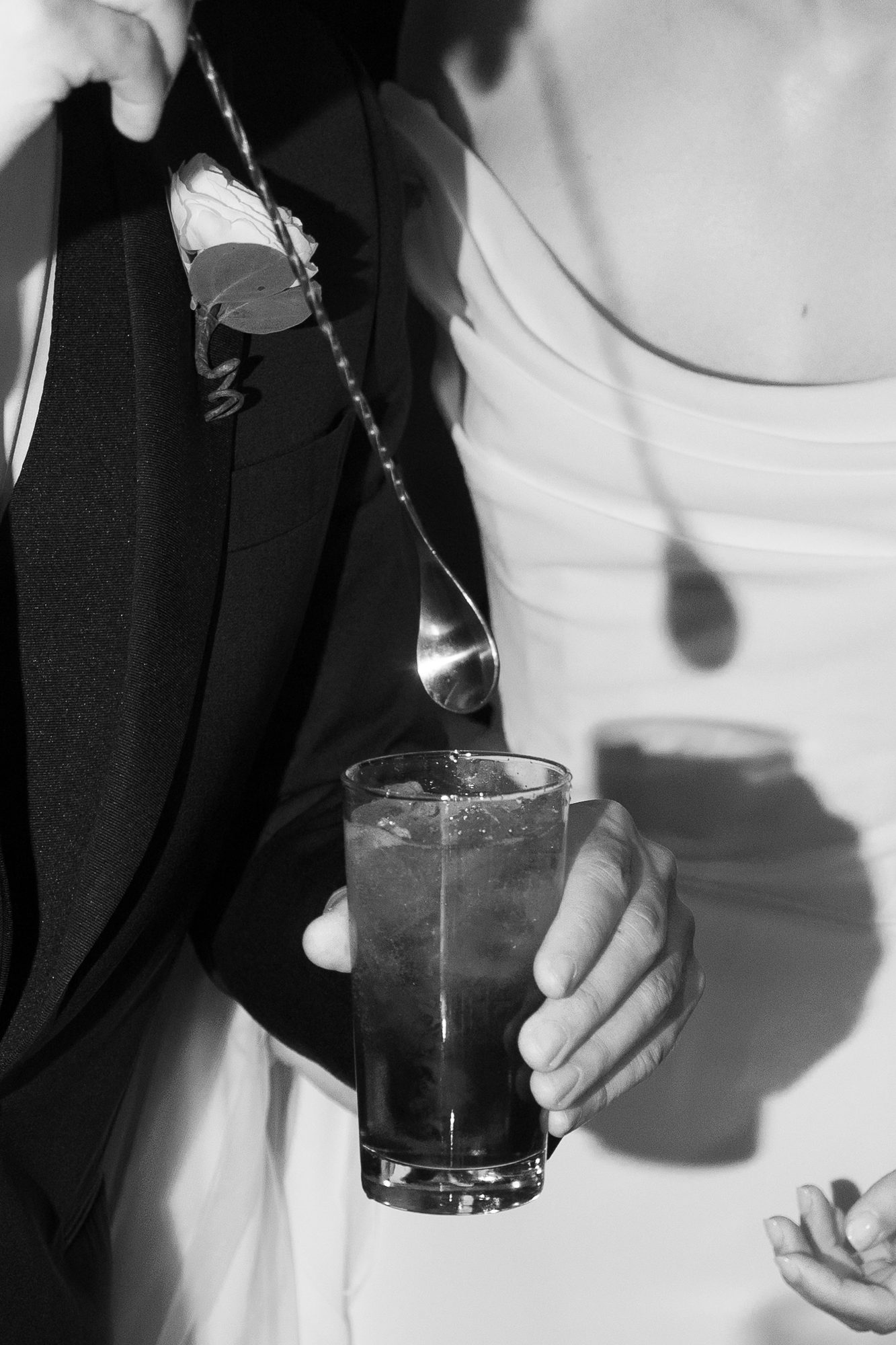 Close detail of a hand holding a drink with ice, a boutonniere visible above it.