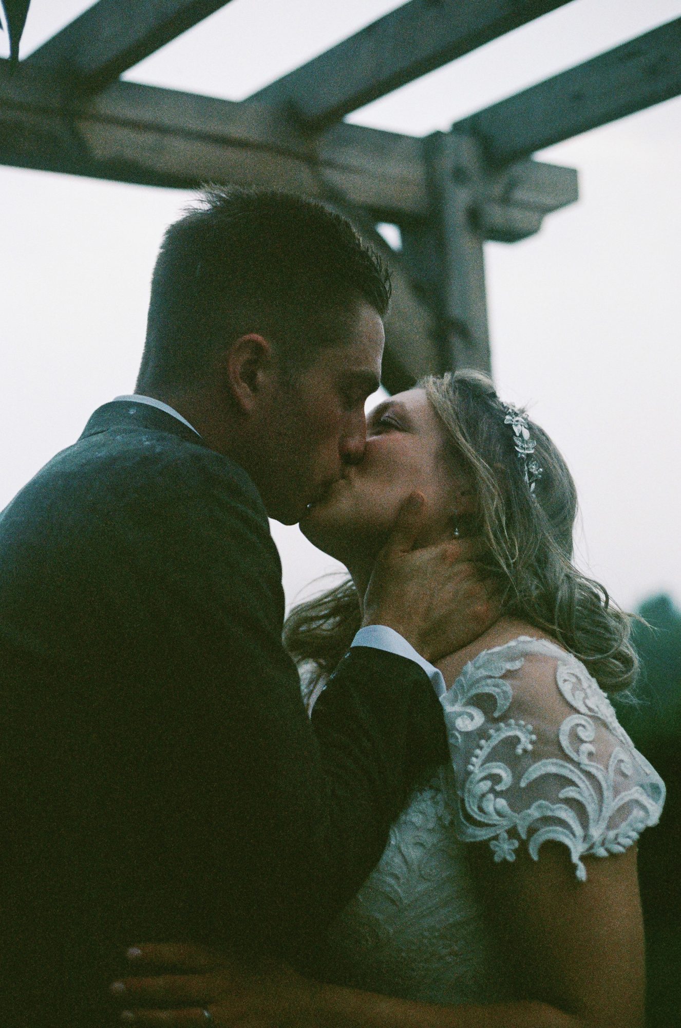 A couple kissing under a wooden pergola at dusk, warm film tones.
