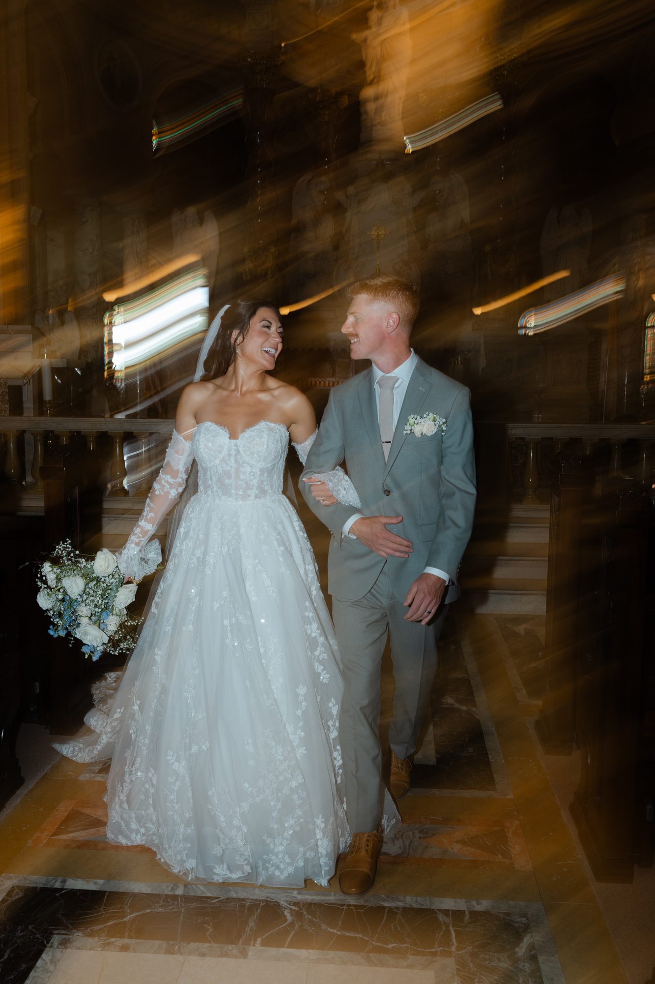 A long-exposure photograph of a bride and groom laughing together on the steps of a cathedral.