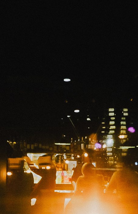 Blurred, warm city lights seen through a car window at night, passengers in silhouette in the foreground.